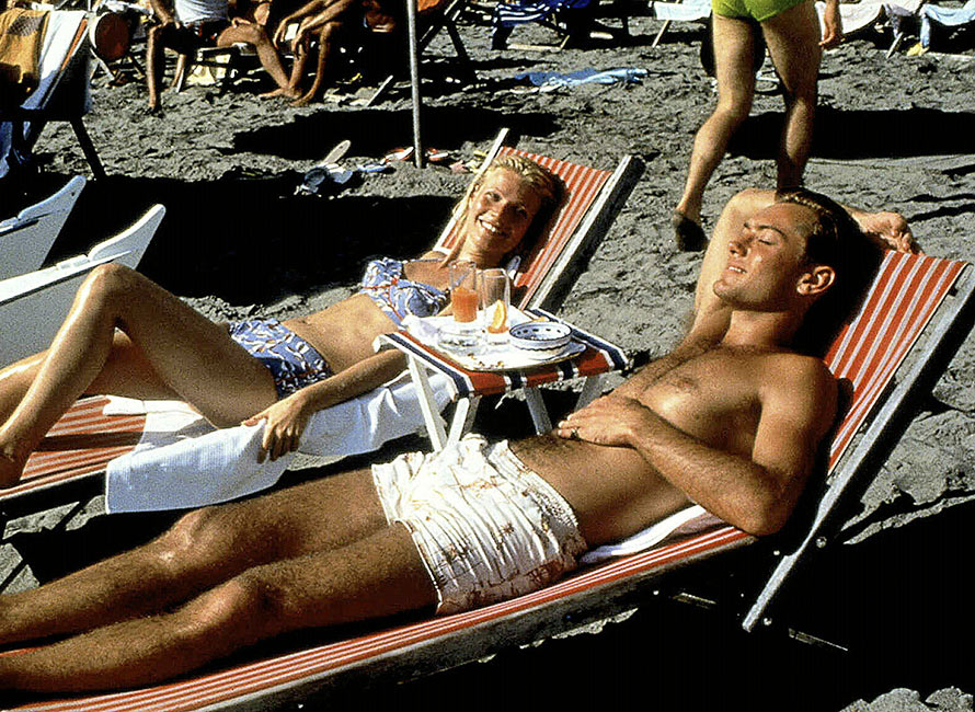 Jude Law in costume bianco sdraiato su un lettino in spiaggia