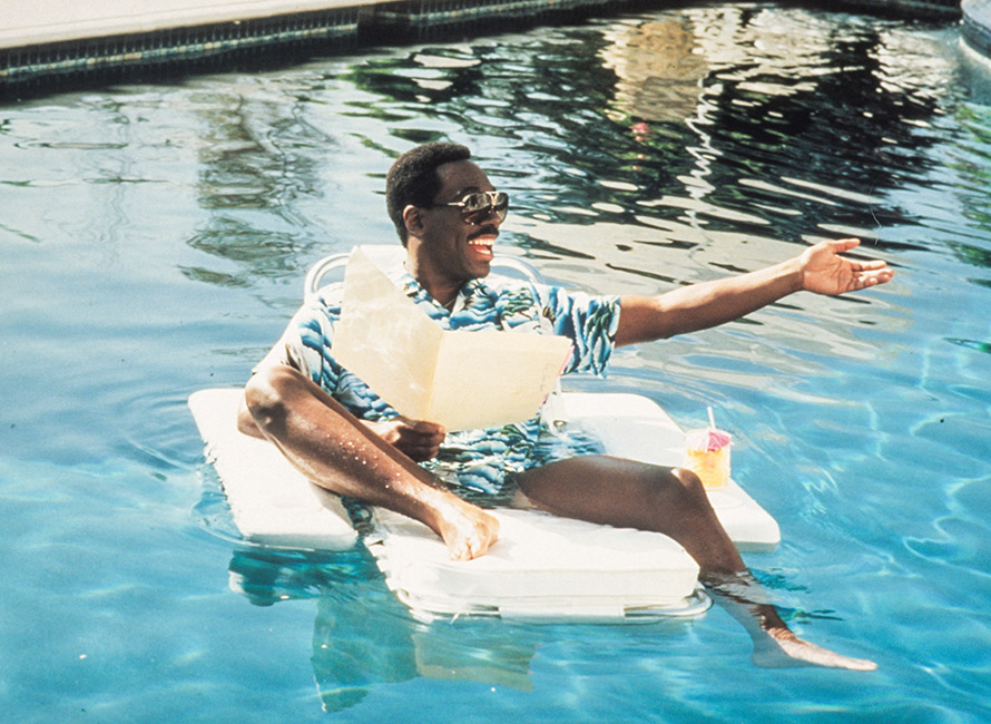 Eddie Murphy in camicia hawaiana e occhiali da sole su una sdraio galleggiante in piscina