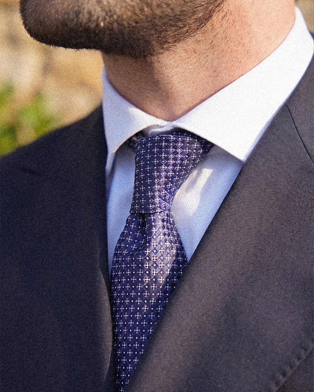 Primo piano di giacca scura, camicia bianca e cravatta blu fantasia