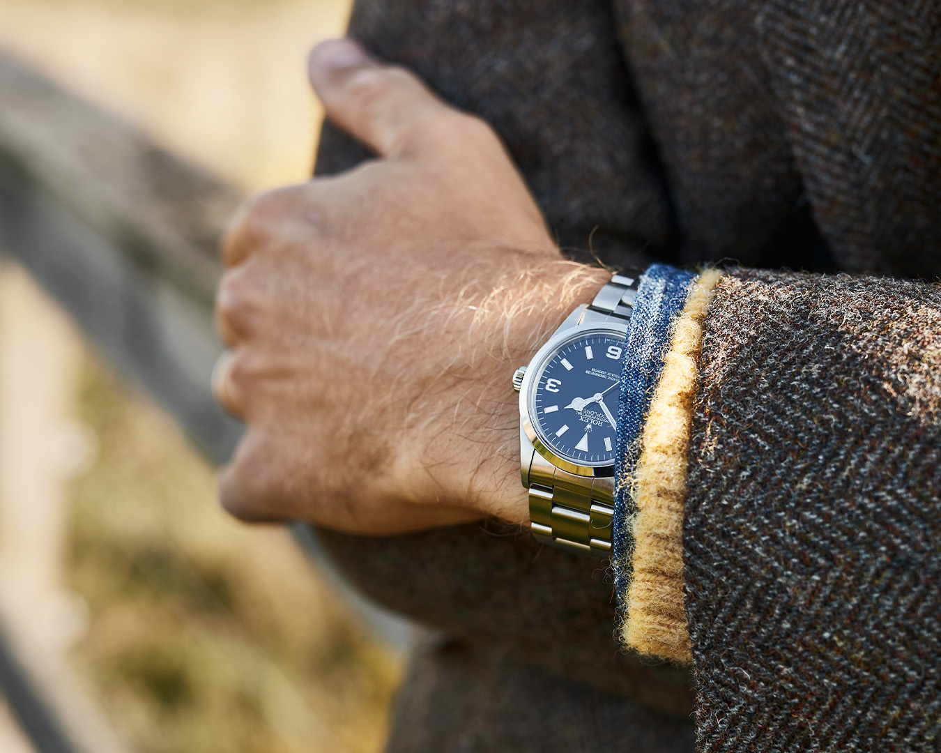 Primo piano di un orologio Rolex con quadrante blu al polso sotto una giacca di tweed