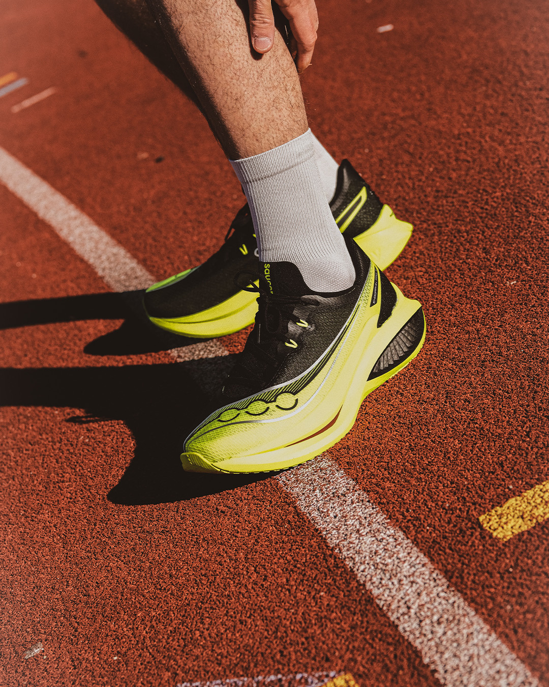 Primo piano di scarpe da running gialle e calze bianche su una pista rossa