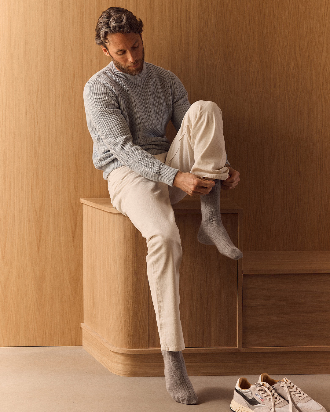 Uomo in maglione azzurro che si infila le calze accanto a un paio di sneakers