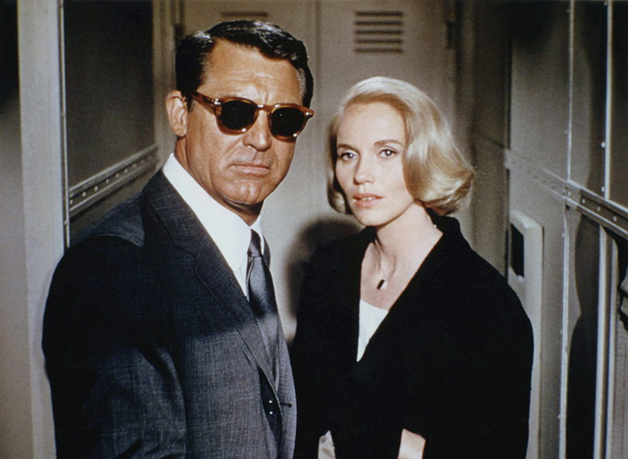Cary Grant con occhiali da sole e abito accanto a una donna vestita di nero