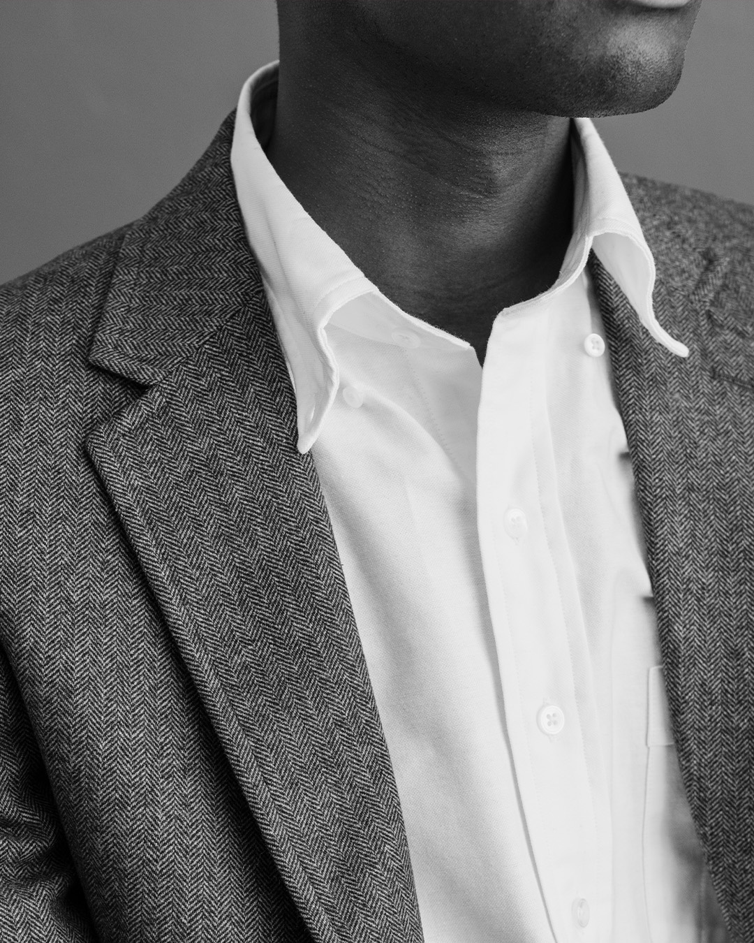 Primo piano in bianco e nero di un uomo in camicia oxford bianca con collo button down e giacca di tweed grigia