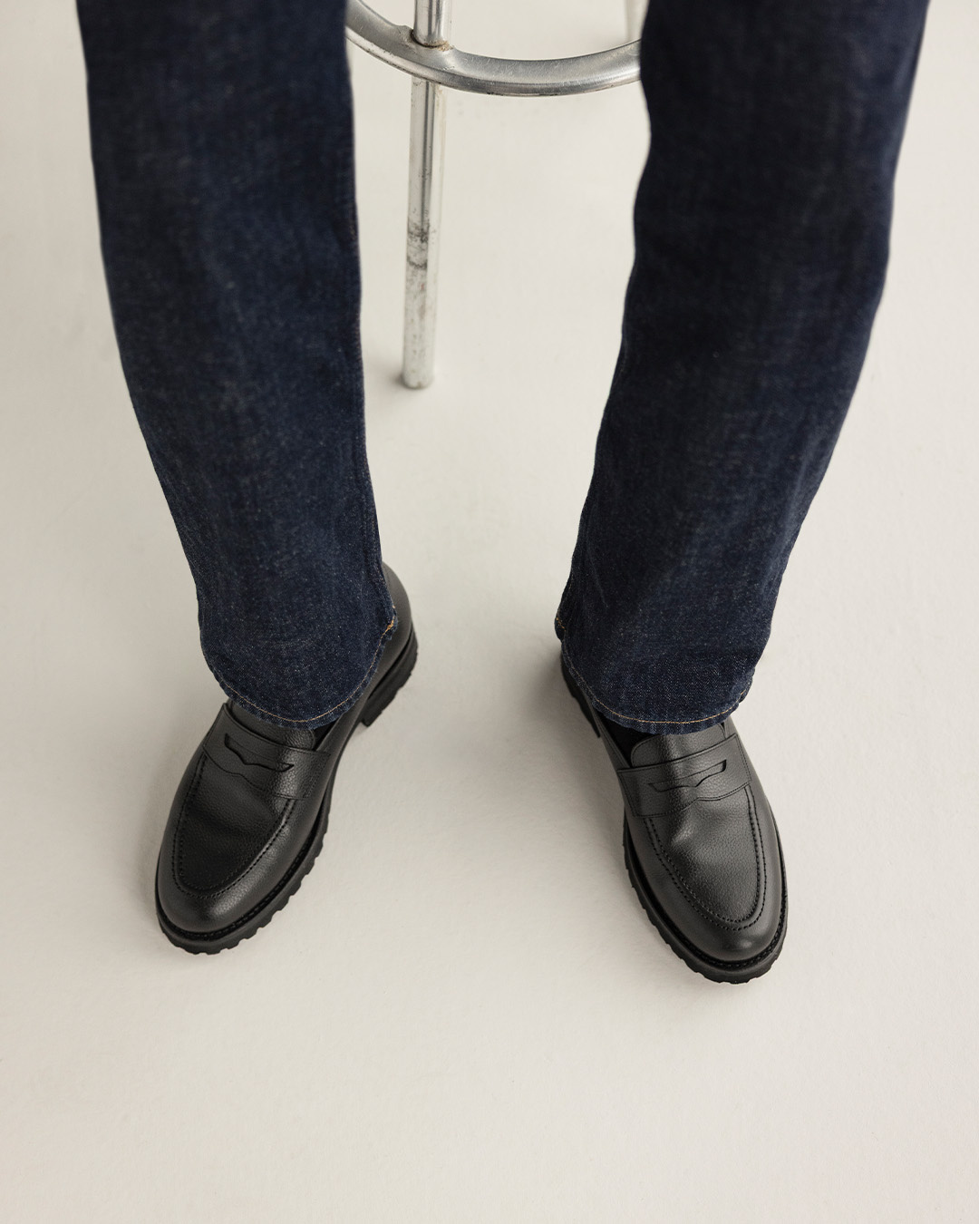 Primo piano di mocassini neri e jeans scuri accanto a uno sgabello