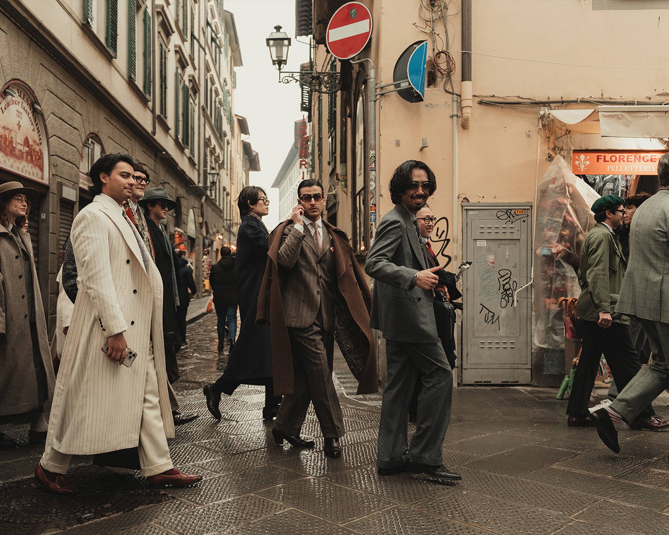 Uomini in cappotti lunghi e abiti che camminano lungo una strada bagnata di pioggia a Firenze