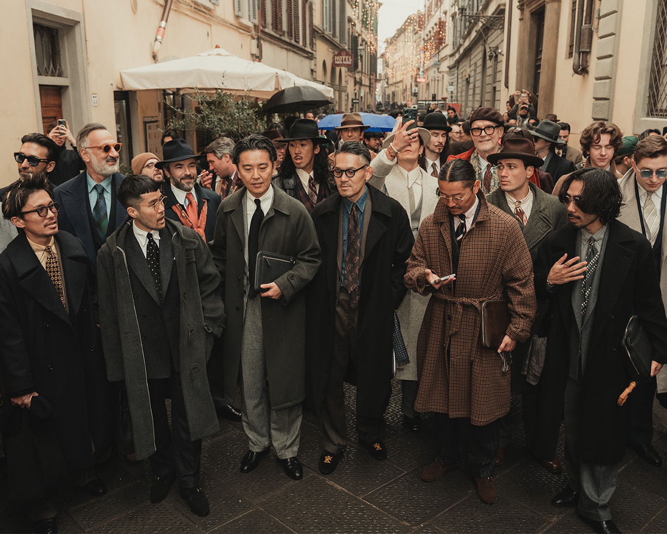 Grande gruppo di uomini in cappotti, abiti e cappelli in una strada di Firenze durante The Suit Walk