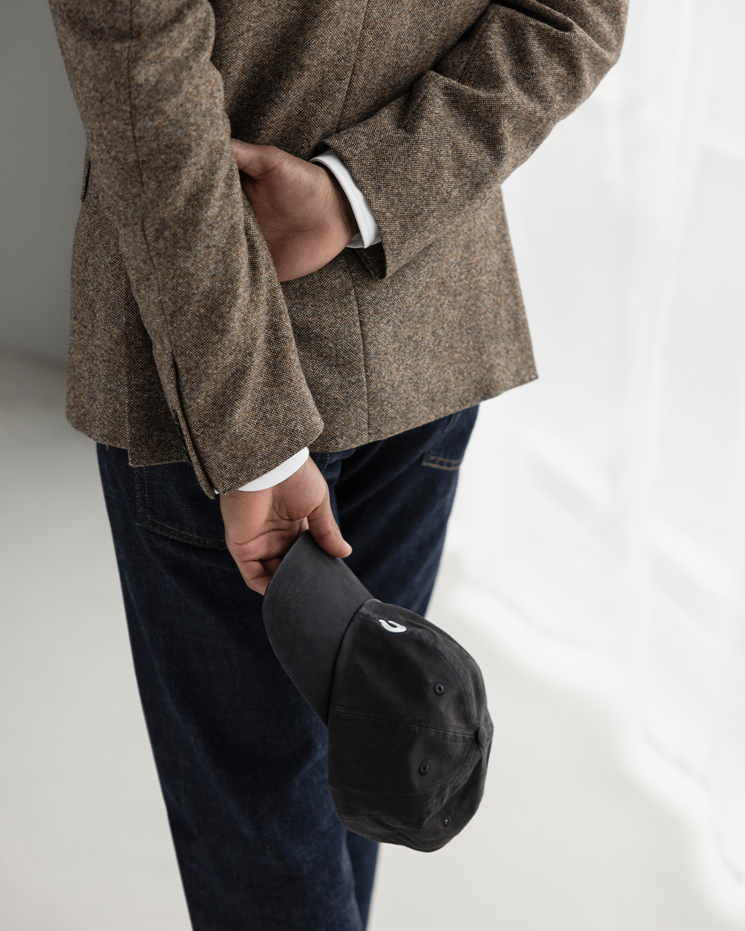 Primo piano di una mano con un cappellino nero contro una giacca marrone e jeans scuri