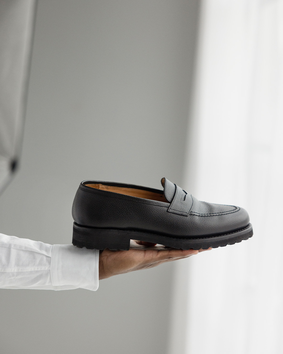 Mano che regge un mocassino nero con robusta suola Vibram