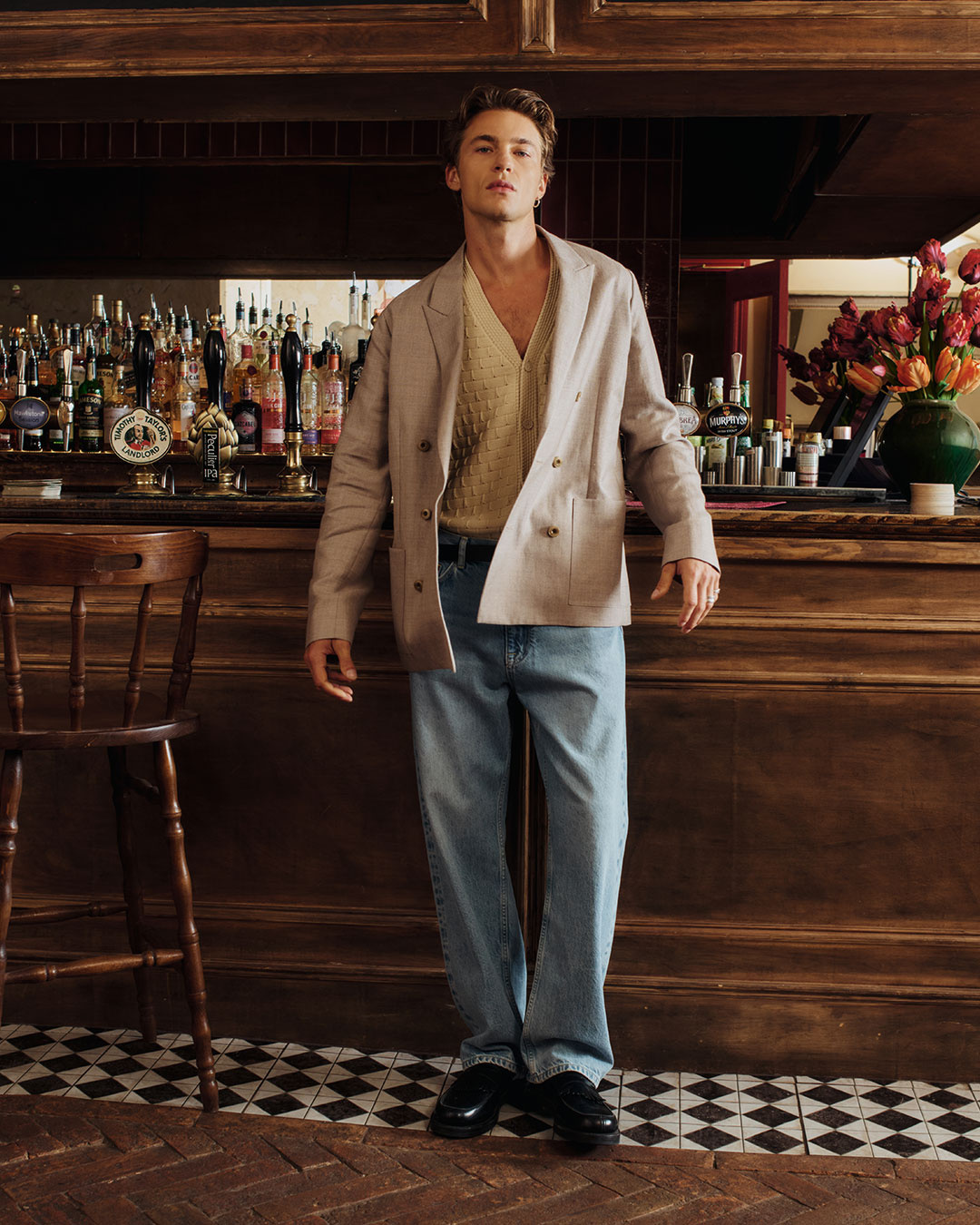 Uomo in giacca beige e jeans chiari in piedi accanto a un bancone bar