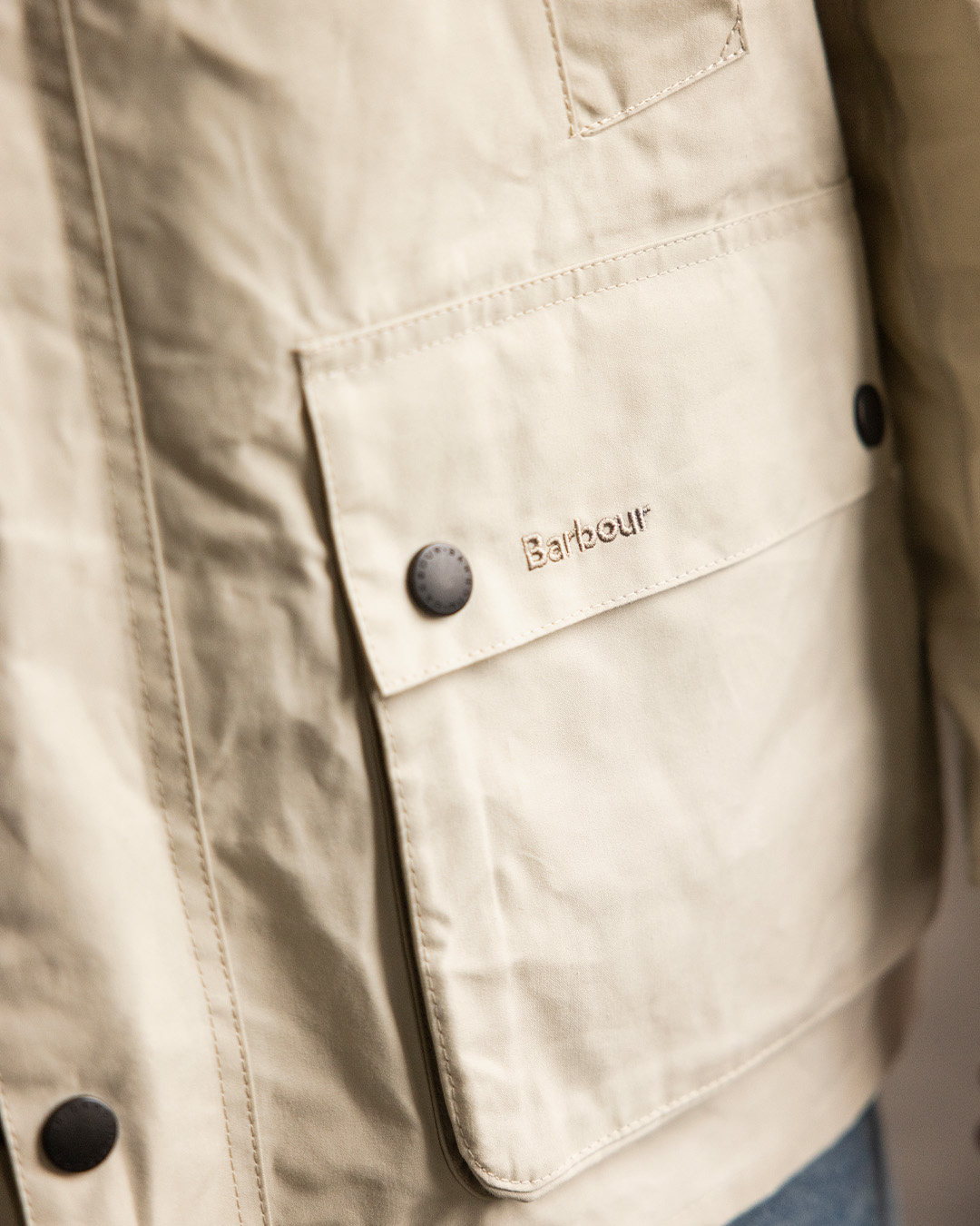 Primo piano di tasca e bottoni automatici di una field jacket beige di Barbour
