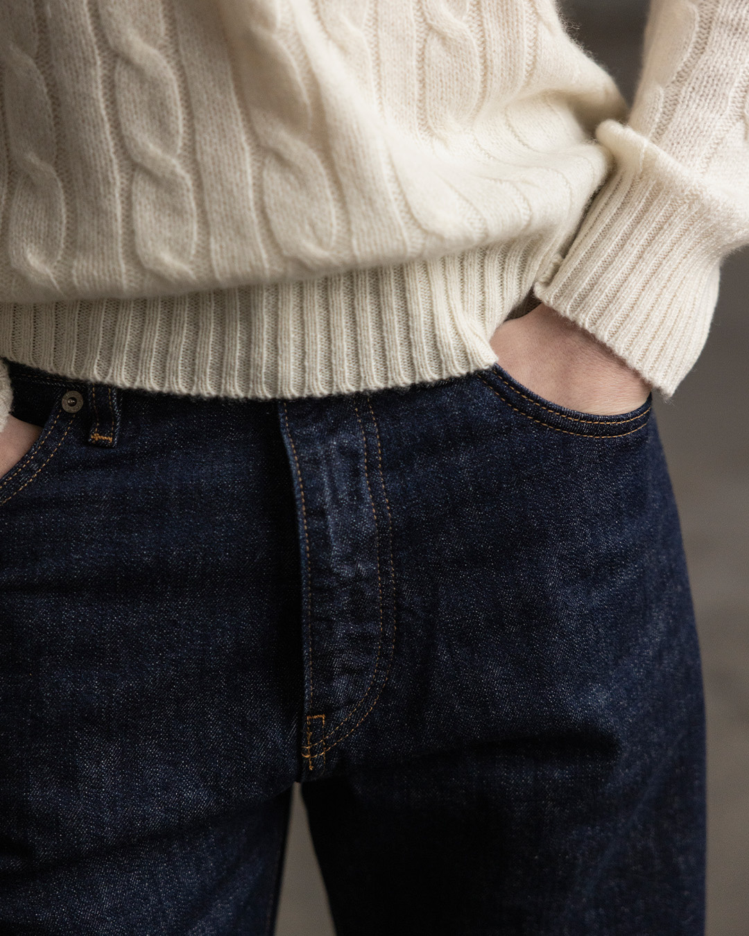 Primo piano di un maglione a trecce color crema e jeans scuri