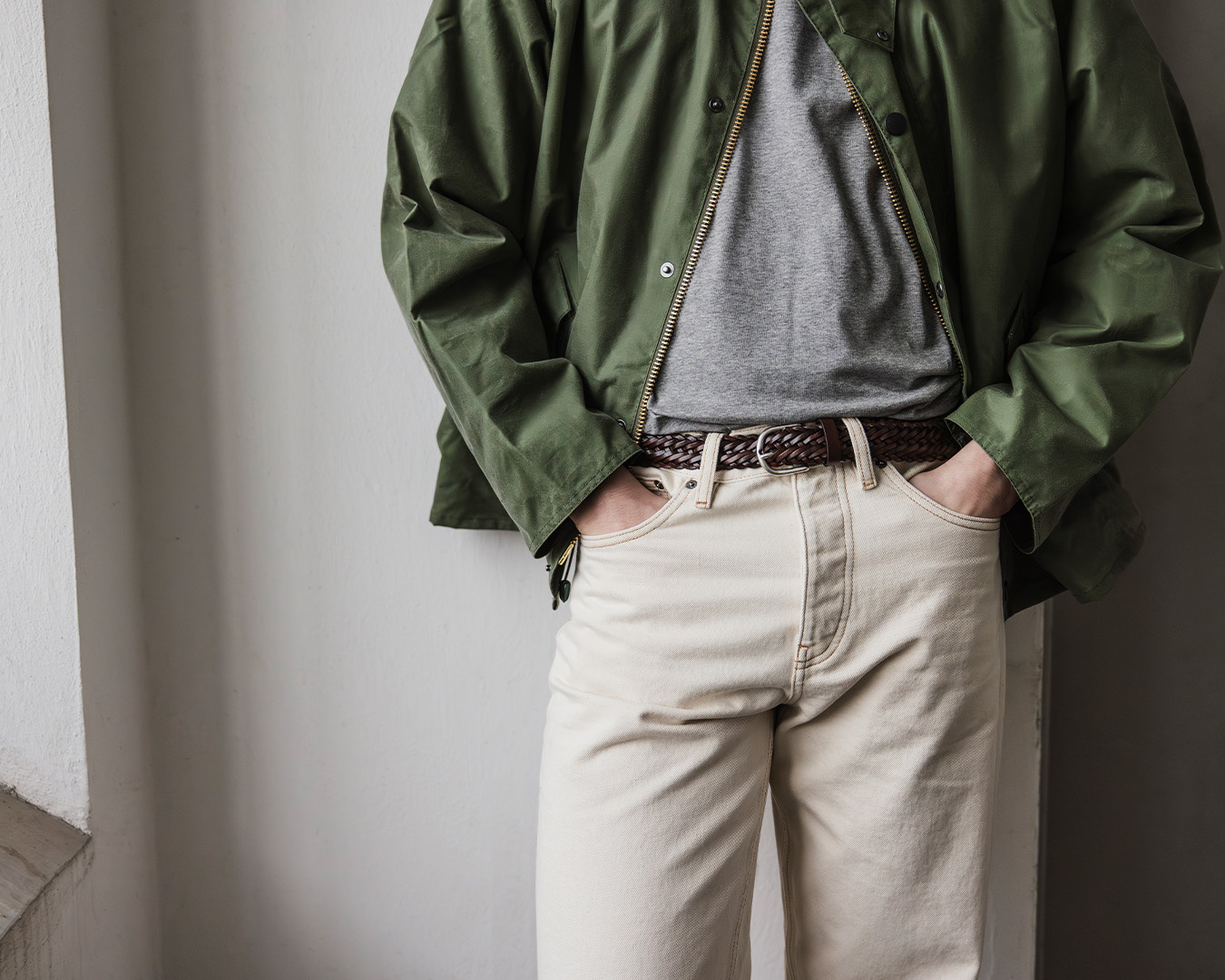 Uomo in giacca verde, t-shirt grigia, cintura marrone e jeans chiari
