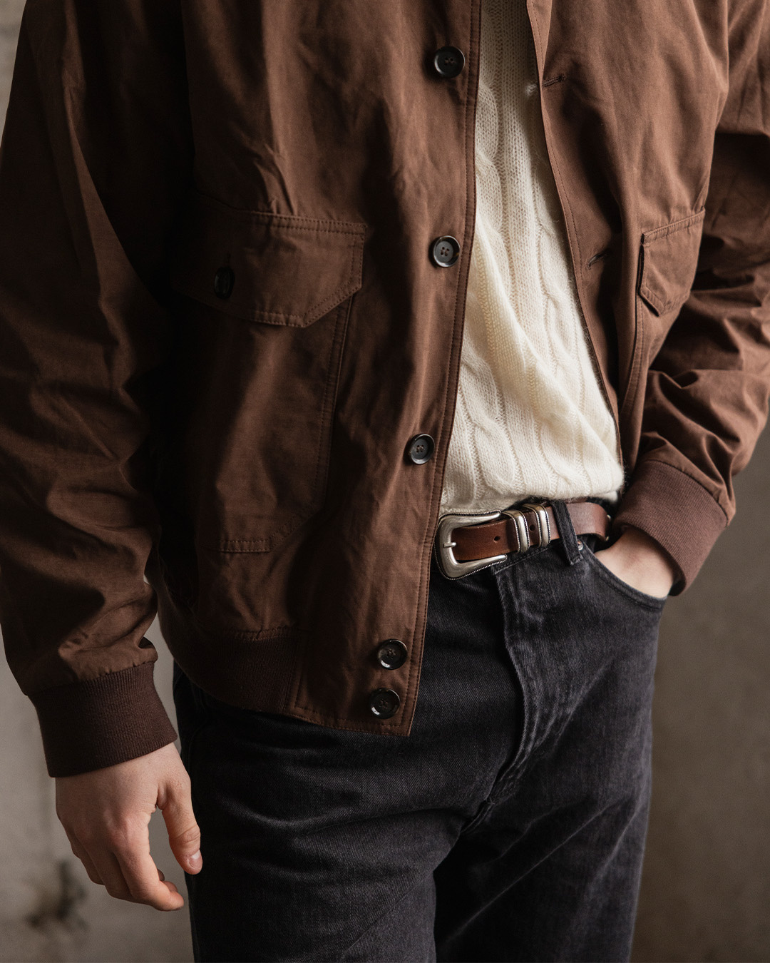 Primo piano di una giacca marrone sopra un maglione bianco crema e jeans neri