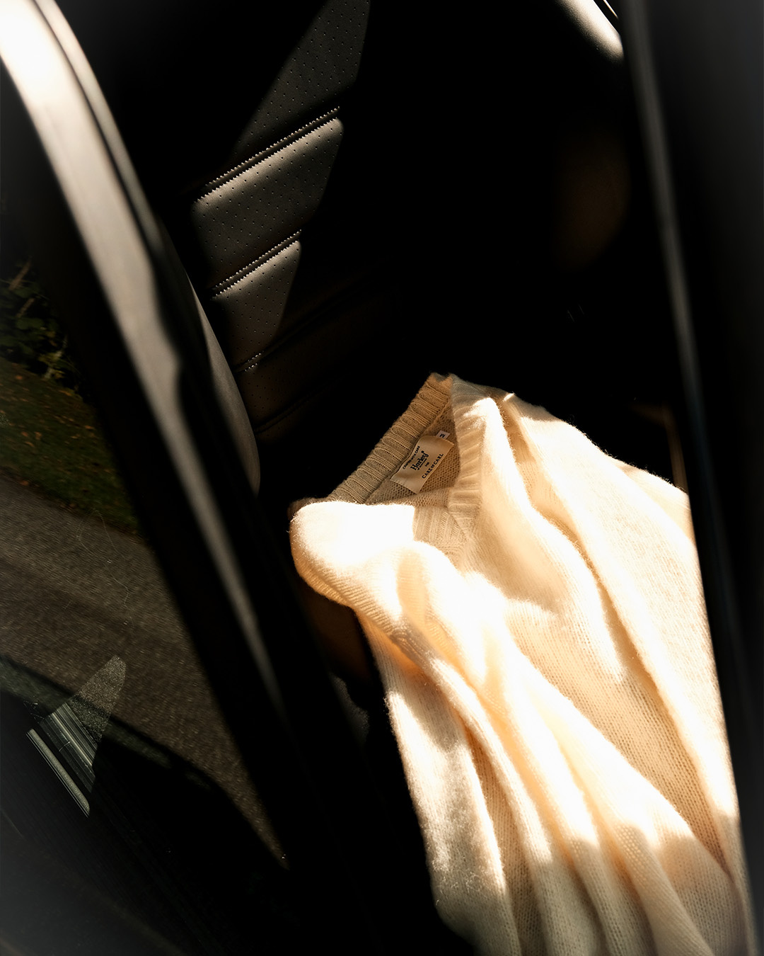 Maglione color crema appeso alla portiera di un'auto