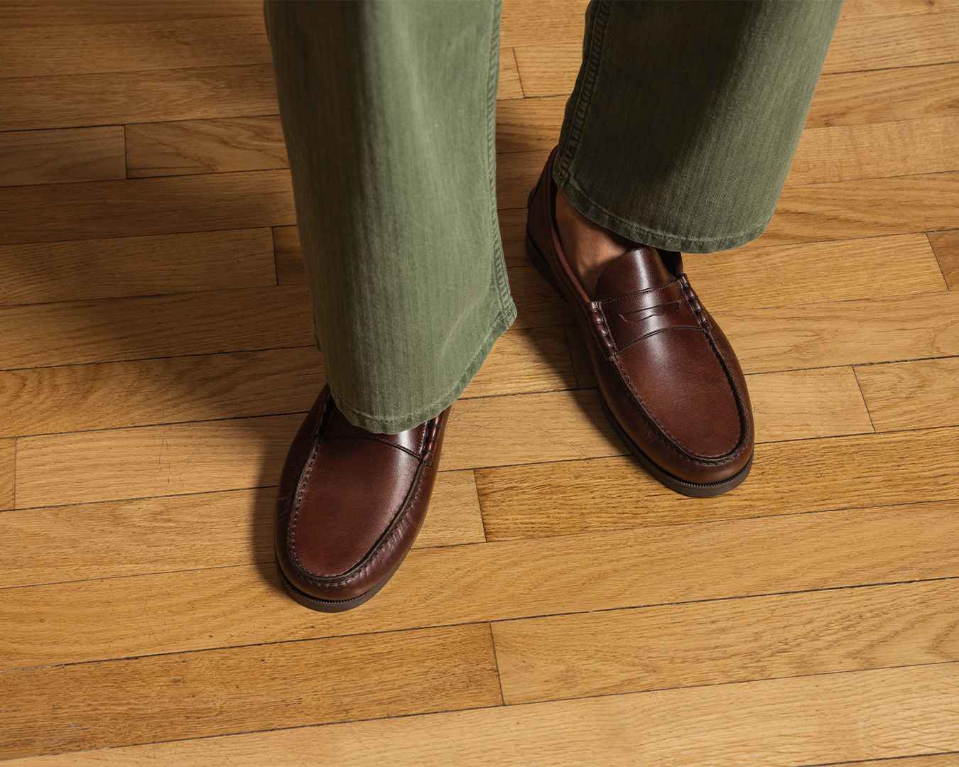 Penny loafer marroni e pantaloni verdi su un parquet