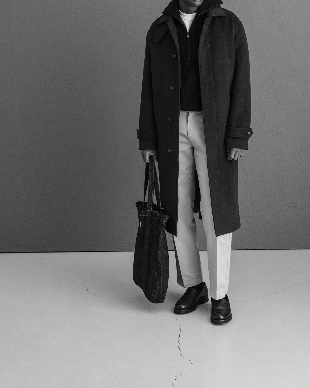 Uomo in cappotto nero, pantaloni chiari e mocassini neri con una borsa