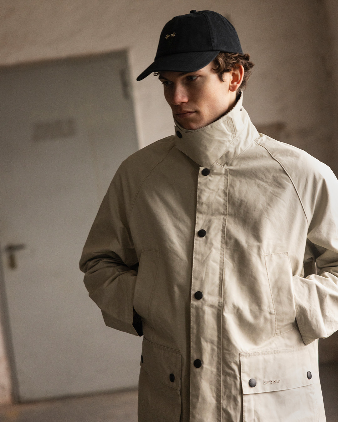 Uomo con cappellino nero e giacca beige a collo alto