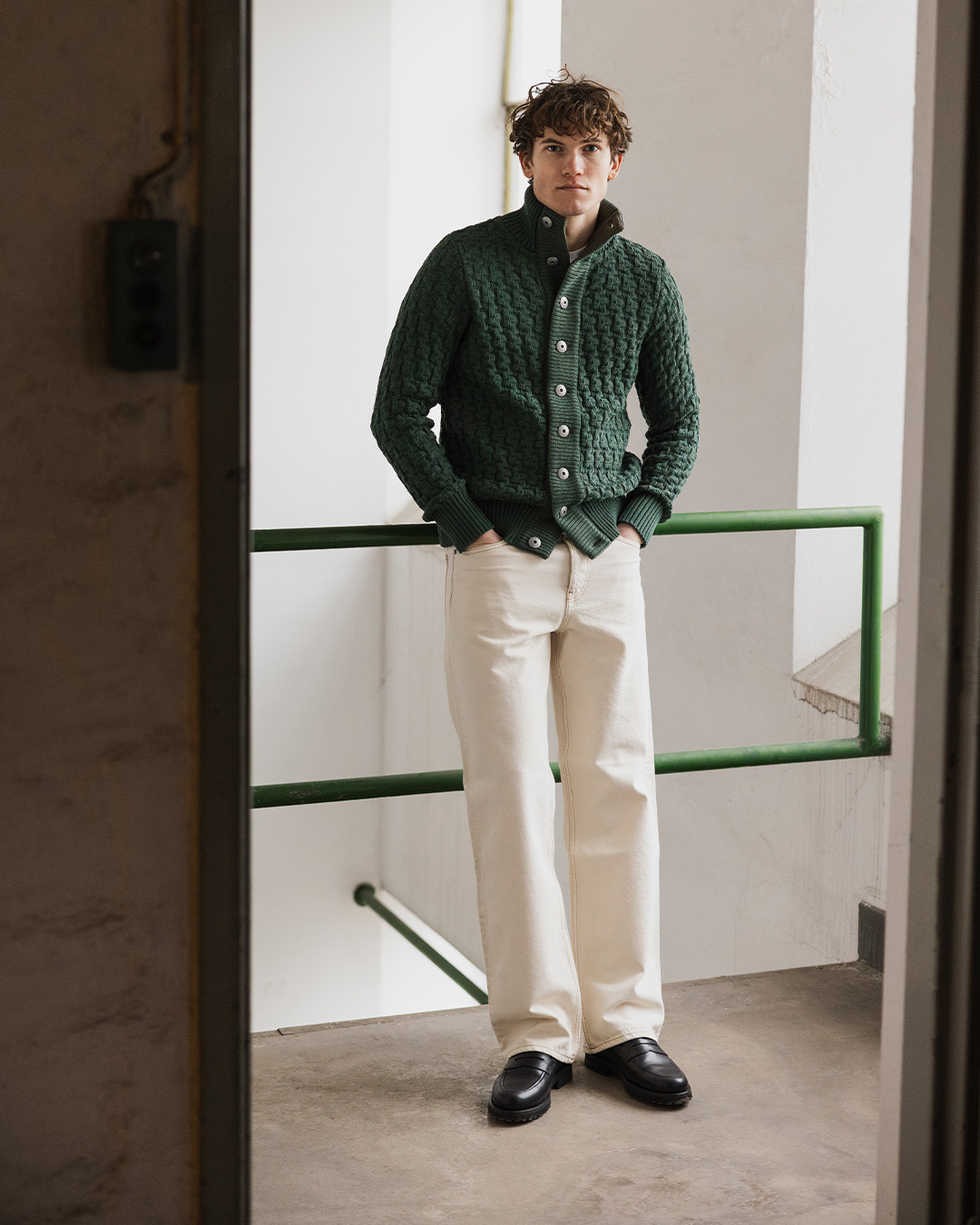 Uomo in cardigan verde, pantaloni chiari e mocassini neri