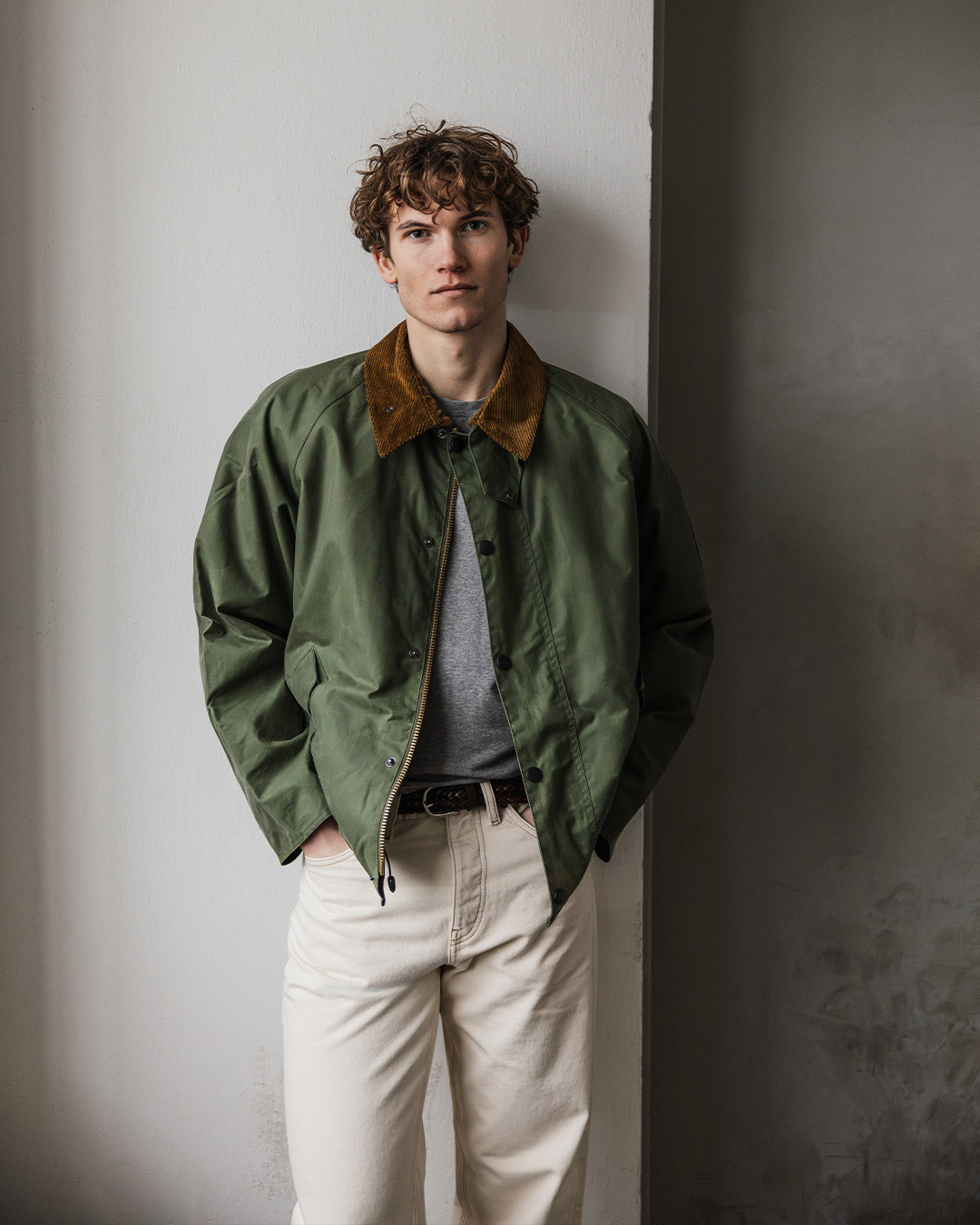 Uomo in giacca verde con collo scuro, maglione grigio e pantaloni chiari