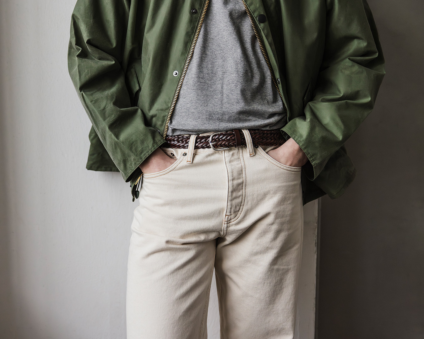 Primo piano di giacca verde, maglione grigio e pantaloni chiari con cintura marrone