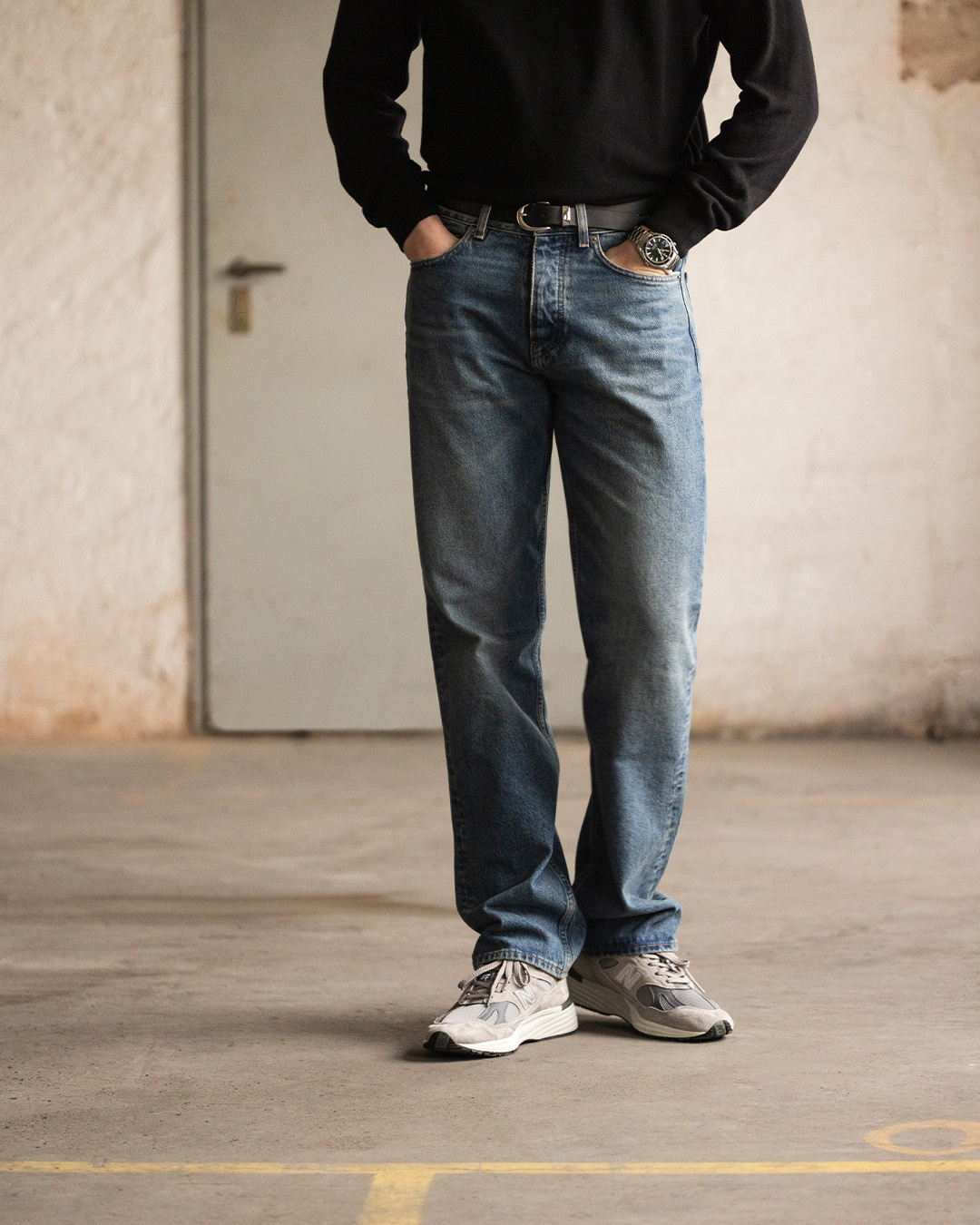 Uomo in maglione nero, jeans blu e sneakers grigie