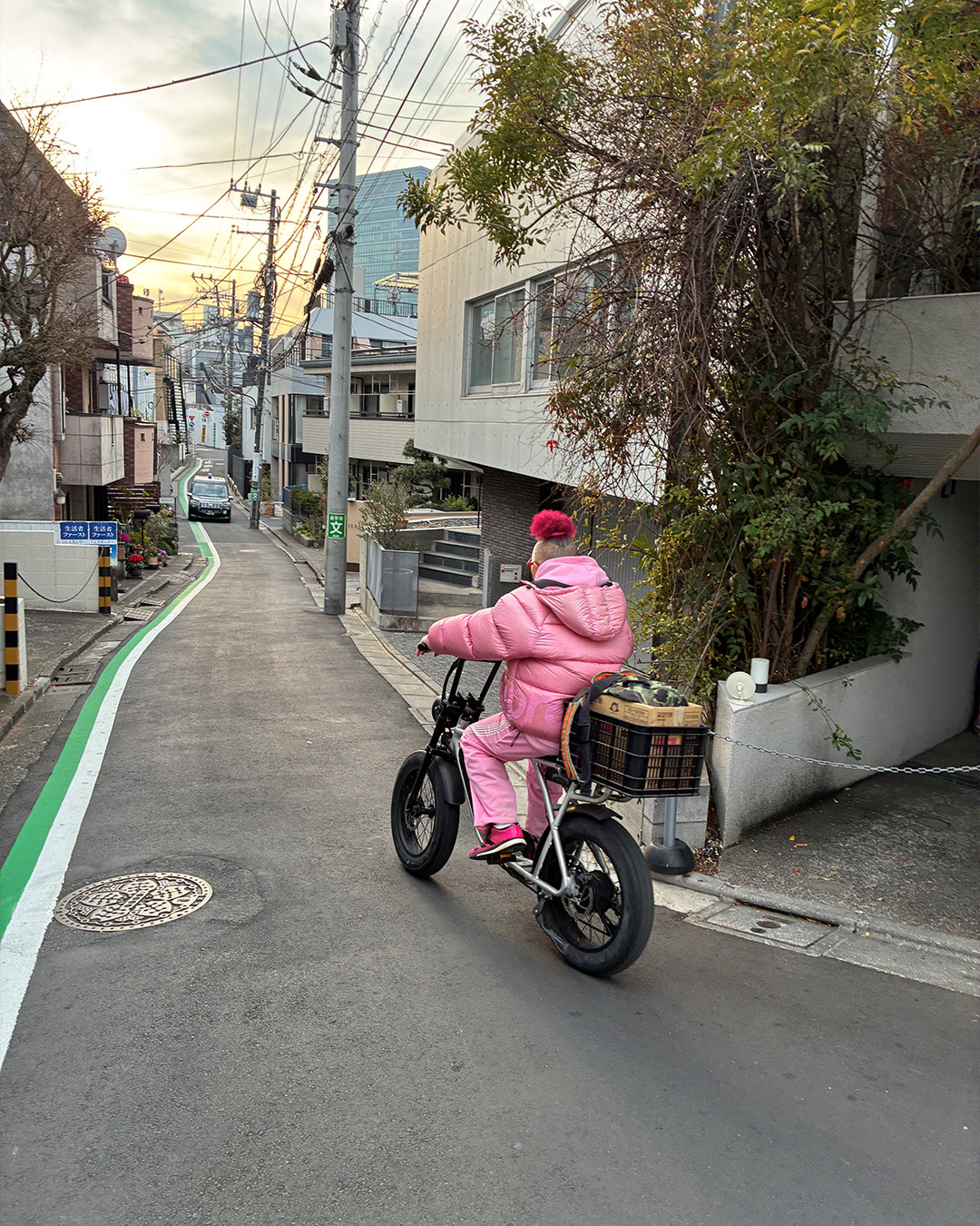 Persona in tuta rosa su una bici elettrica in una stradina di Tokyo