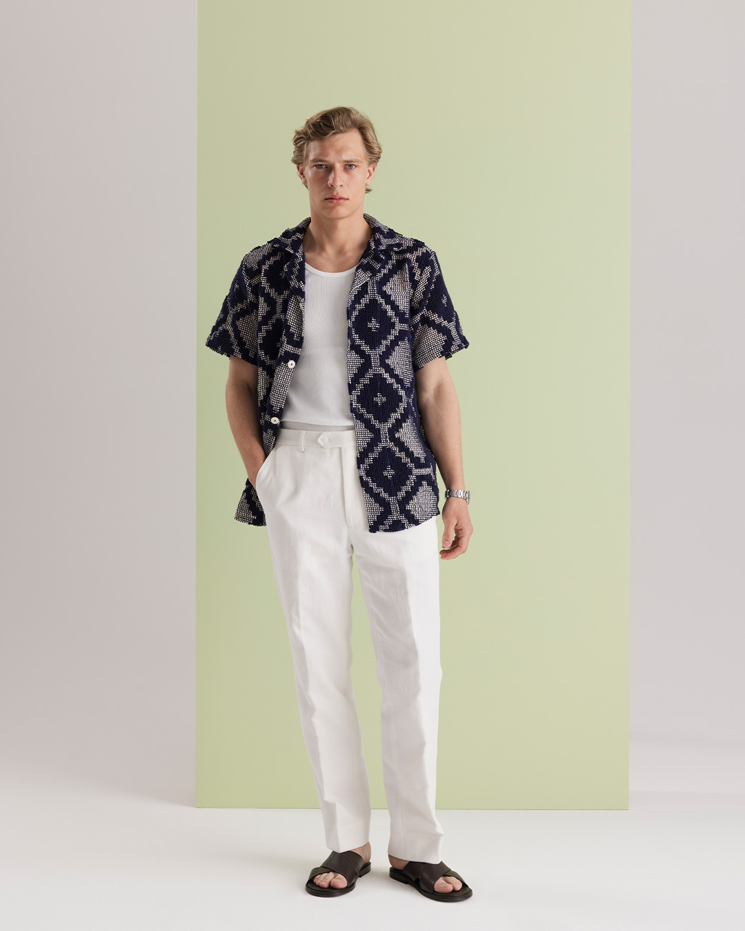 Uomo in camicia resort fantasia, pantaloni di lino bianchi e sandali