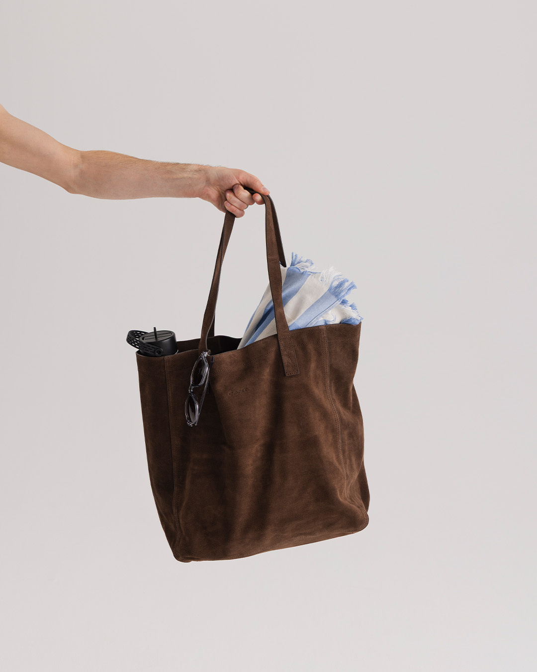 Mano che tiene una borsa in suede marrone con un asciugamano dentro