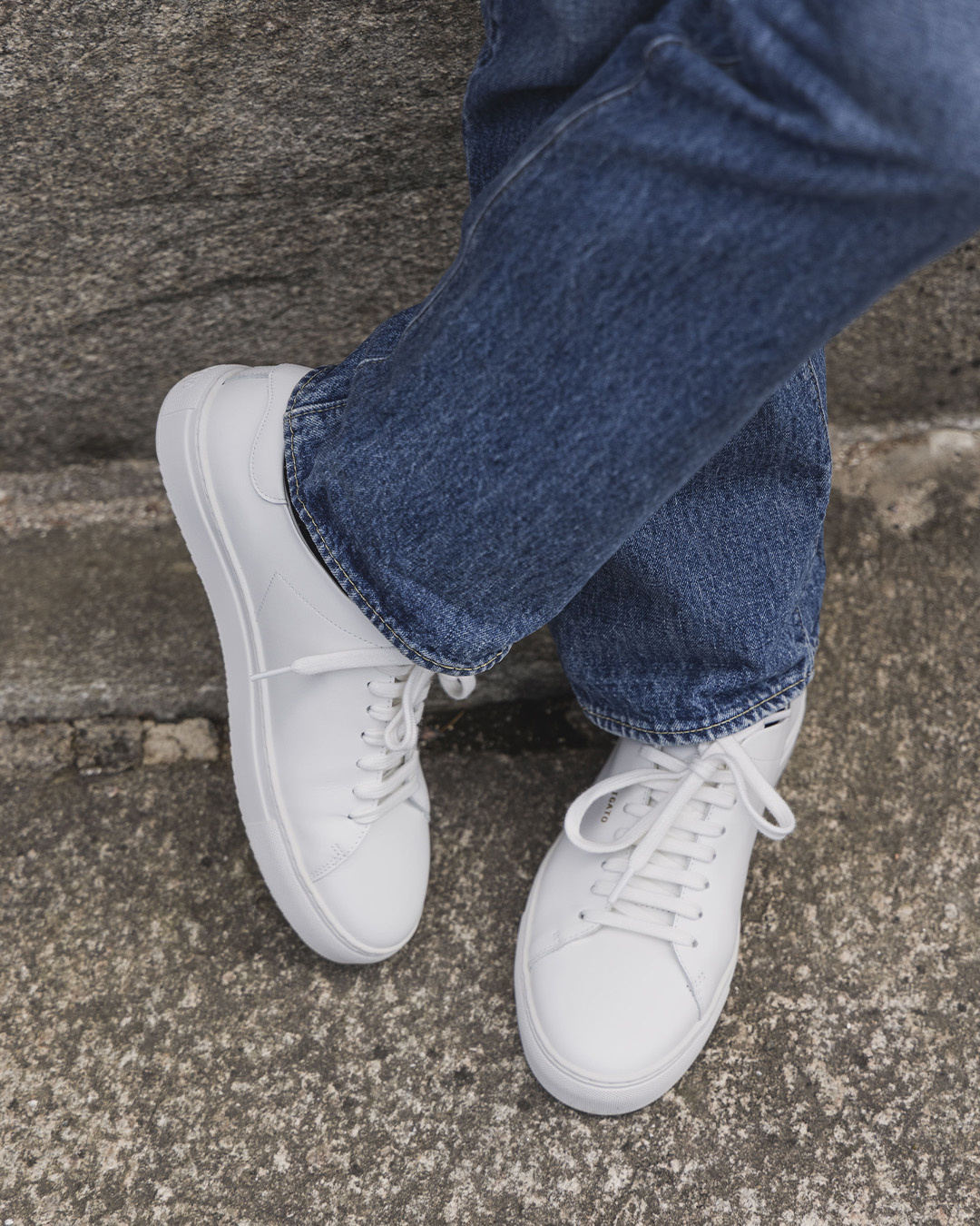 Primo piano di sneakers bianche e jeans blu su una scala di pietra