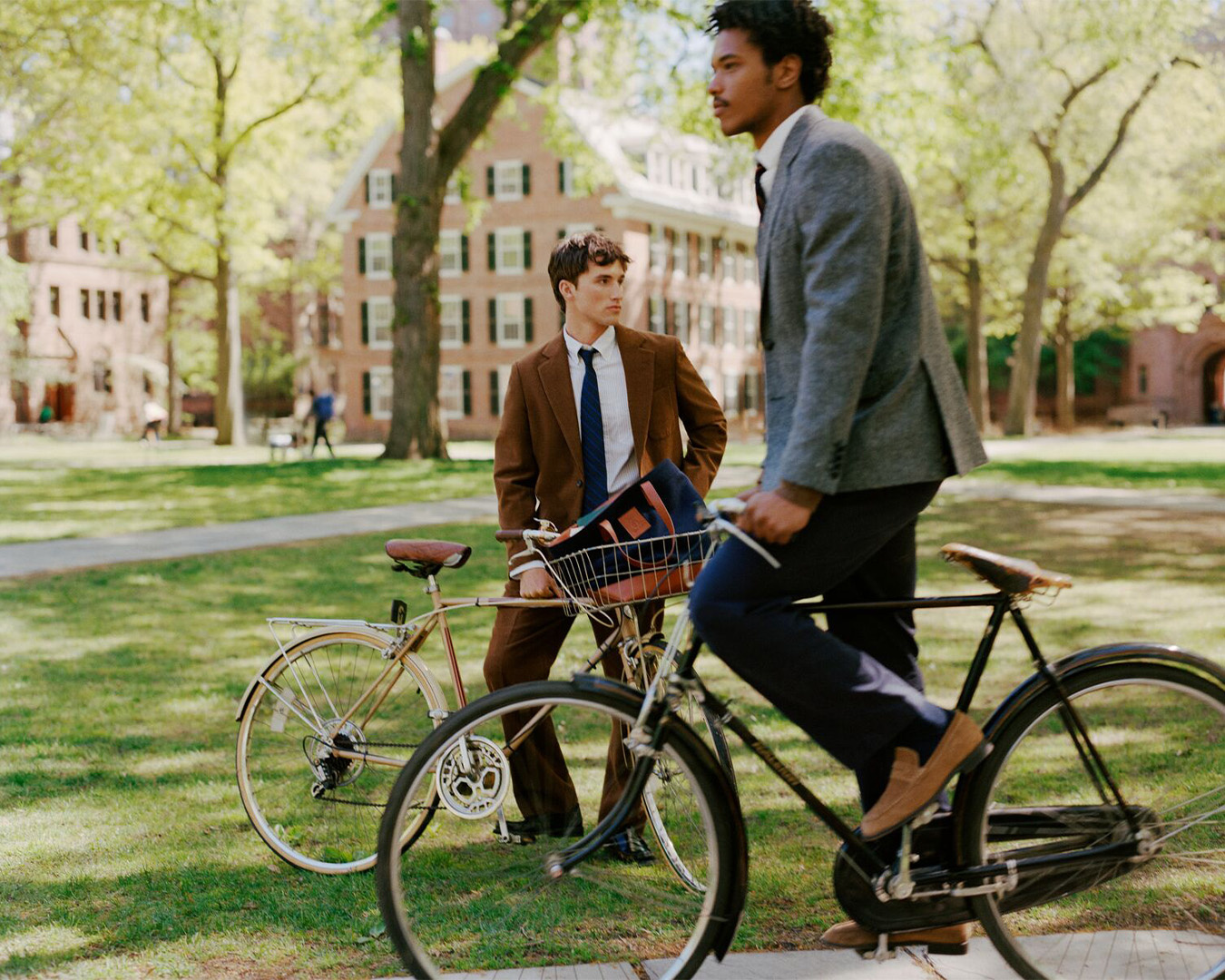 Due giovani uomini in giacca con biciclette in un campus universitario verde