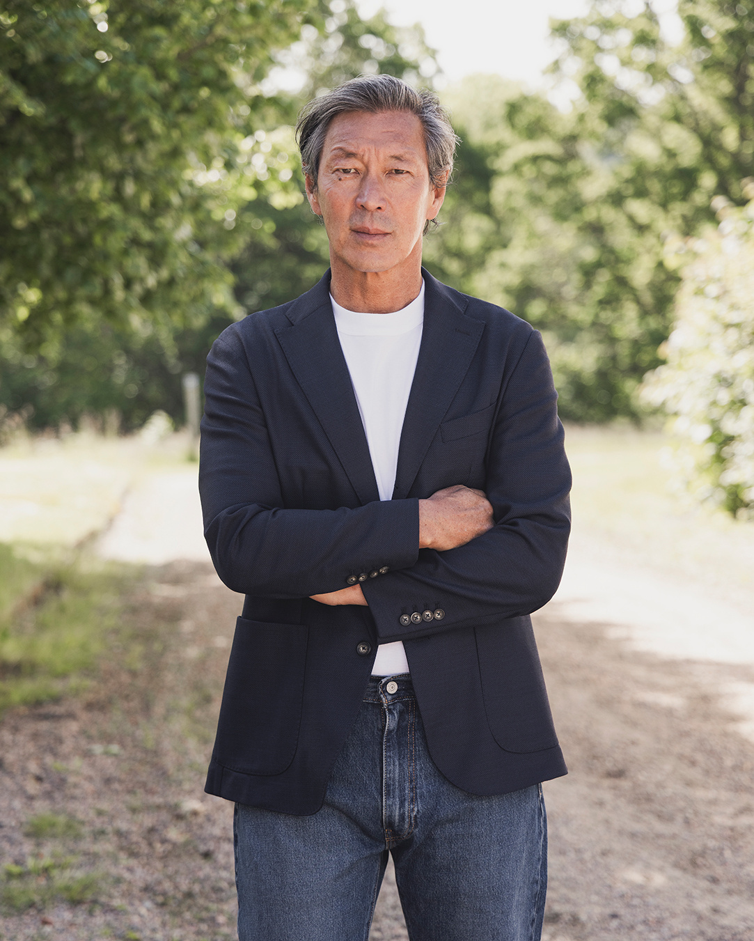 Uomo in giacca blu scuro, t-shirt bianca e jeans a braccia conserte