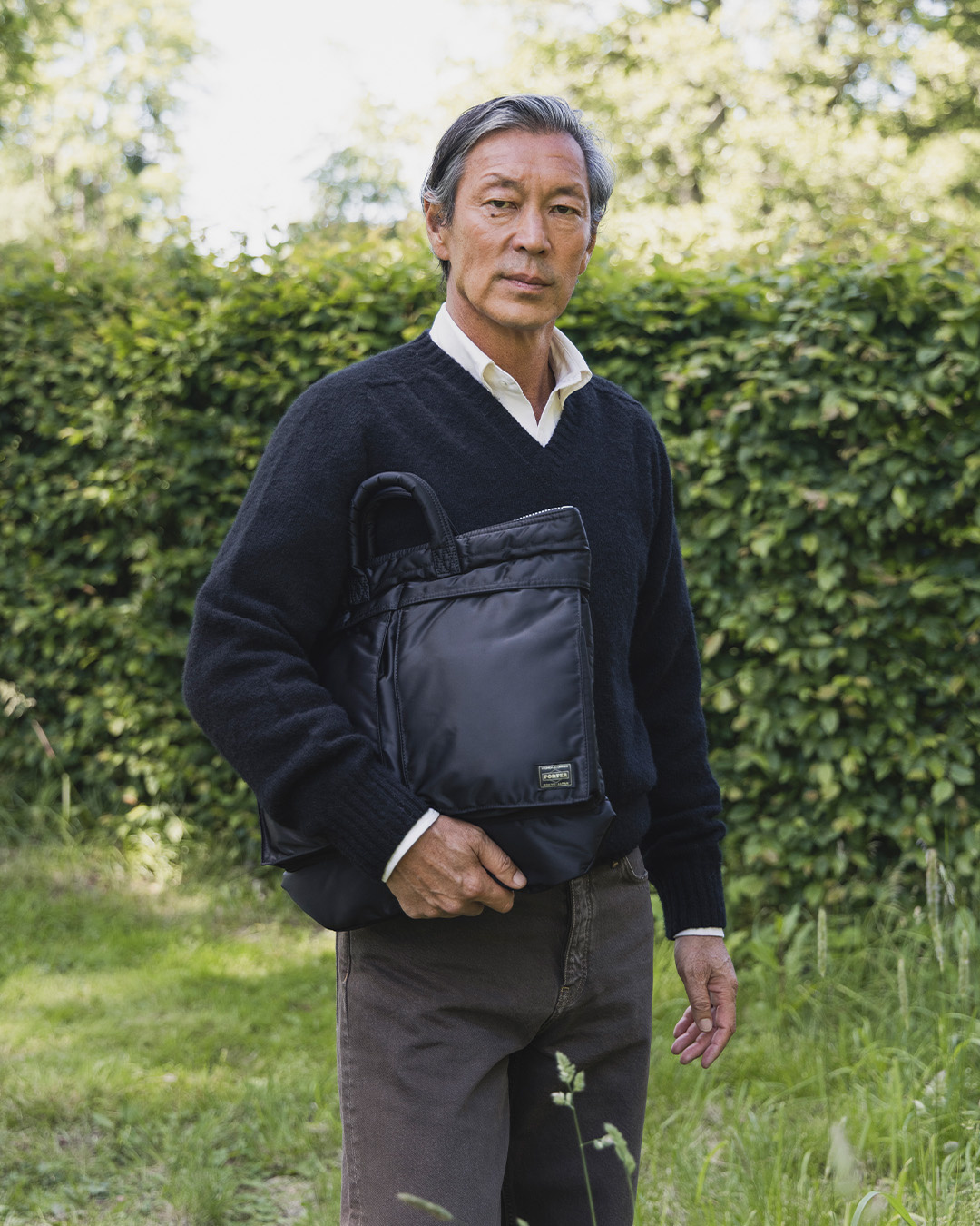 Uomo in maglione blu scuro con una borsa portadocumenti nera sotto il braccio