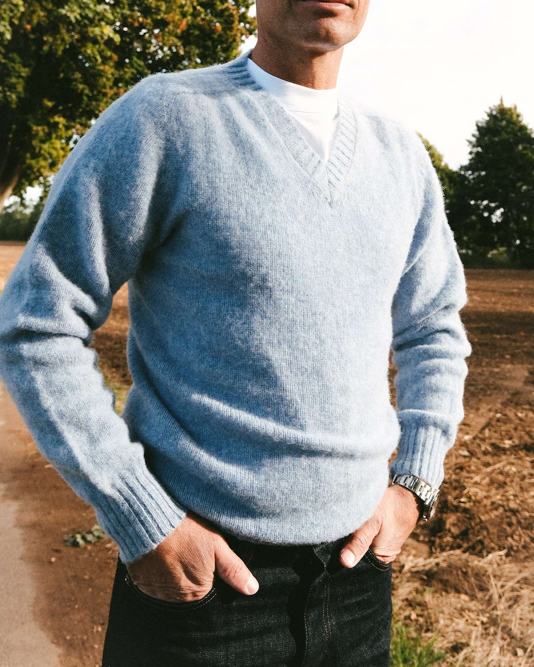 Uomo in maglione azzurro con scollo a V e jeans in un campo