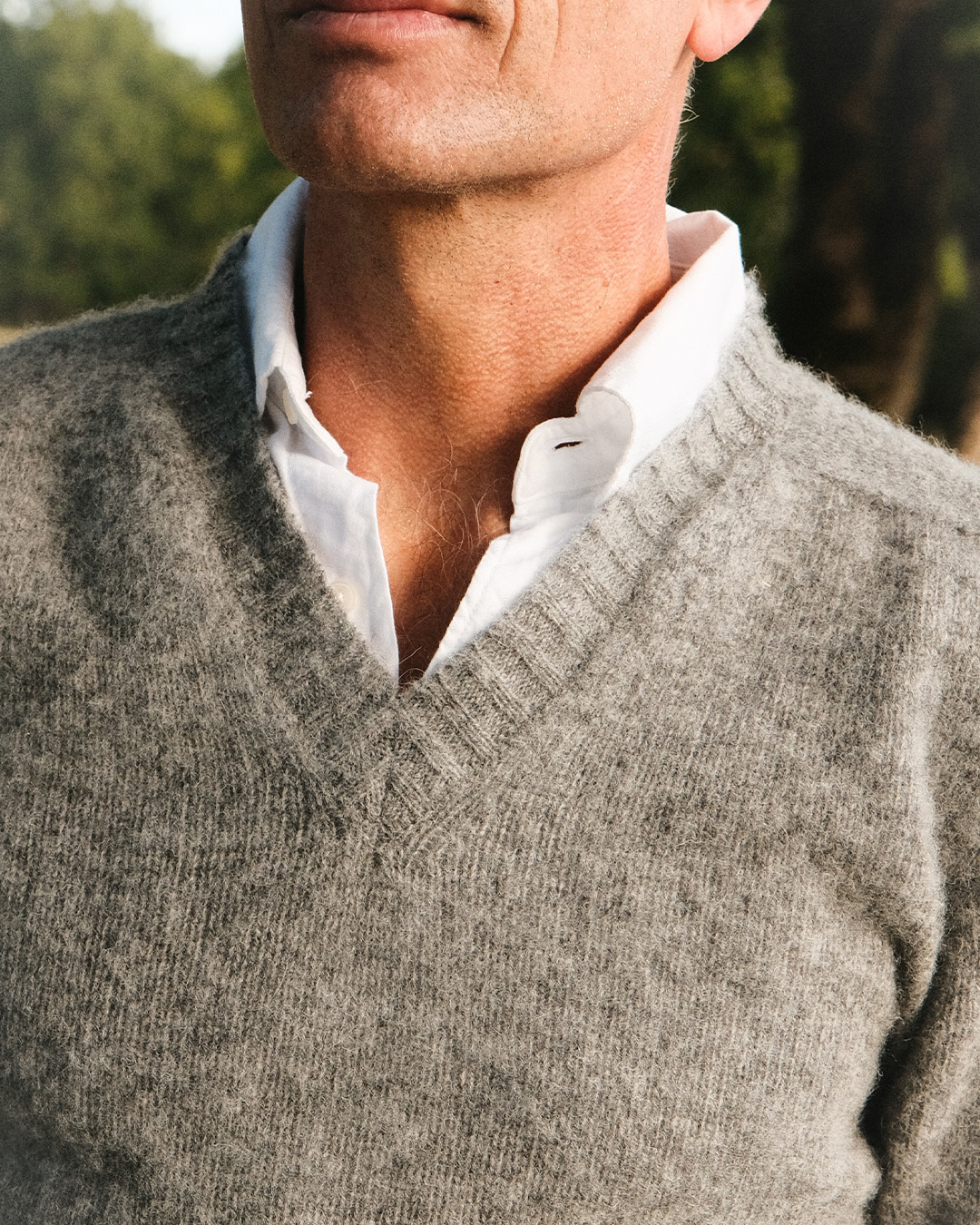 Primo piano di un maglione grigio con scollo a V sopra una camicia bianca